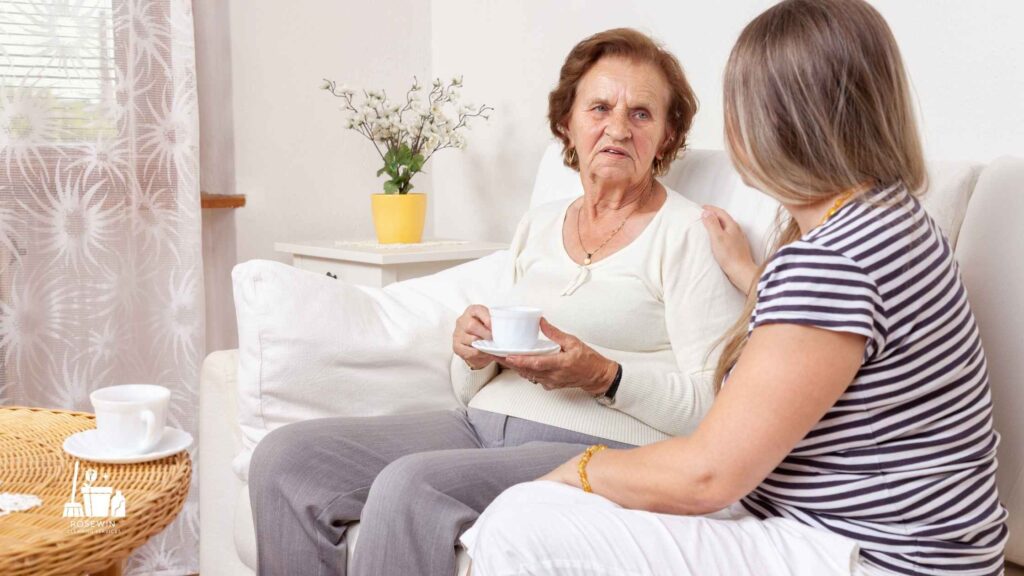 A Rosewin Cleaning Services cleaner comforting an elderly woman over a cup of tea, representing our gentle approach as cleaners for dementia patients.